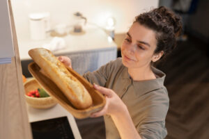 A person holds a freshly baked baguette on a wooden platter, surrounded by a cozy kitchen setting with a bowl of fresh vegetables.