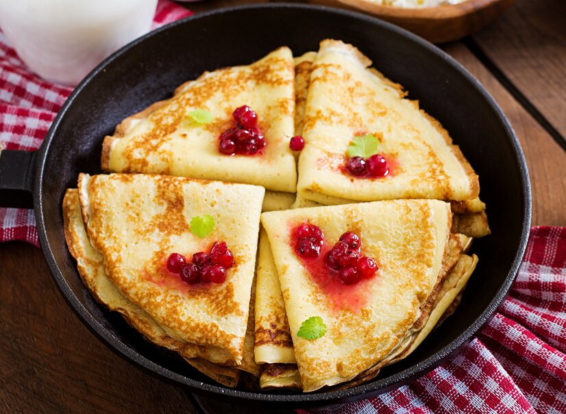 A cast-iron skillet filled with golden, crispy fried potatoes resting on a rustic wooden table, accompanied by a red checkered cloth.