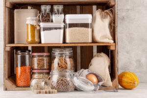 A wooden shelf displays an organized collection of jars and containers filled with grains, spices, legumes, and a small pumpkin.
