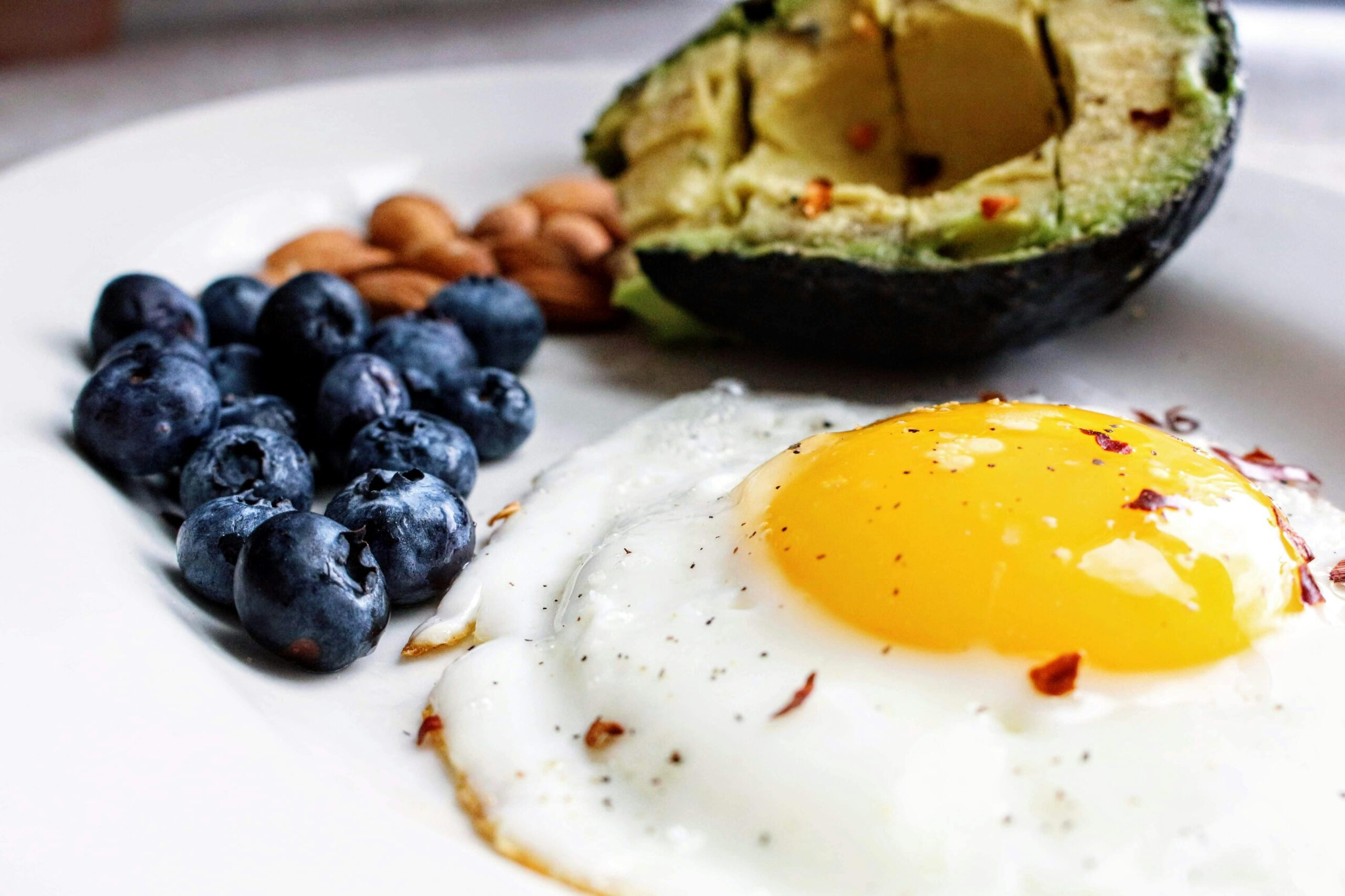 A plate featuring a sunny-side-up egg, fresh blueberries, sliced avocado, and almonds, arranged artfully for a nutritious breakfast.