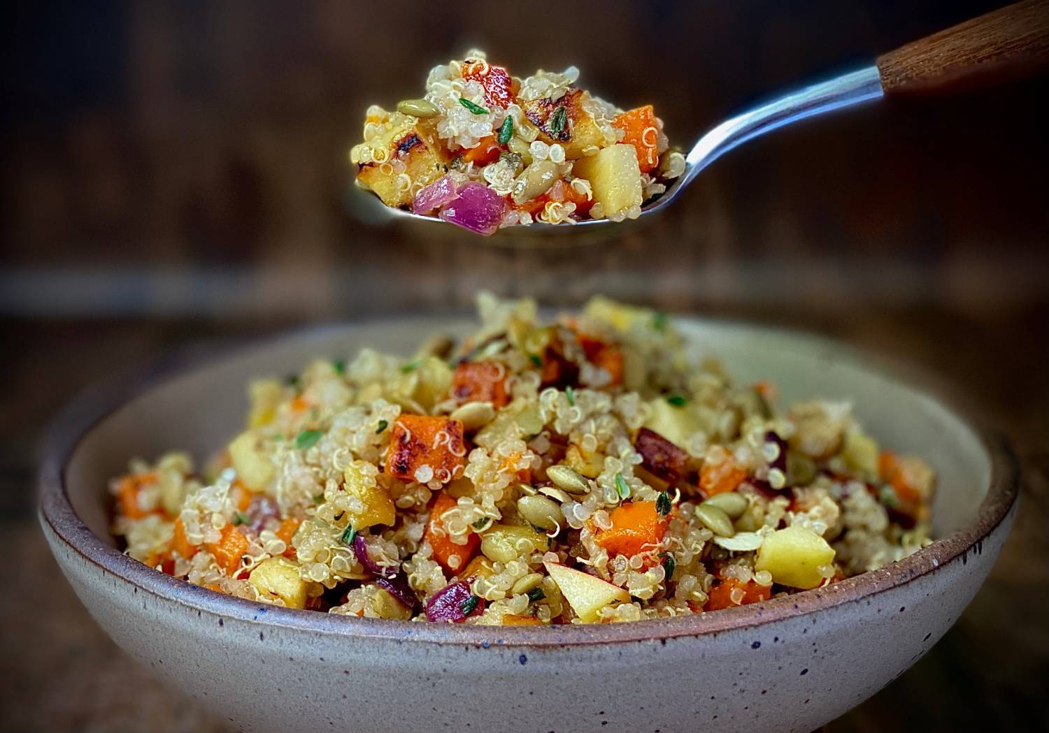 A bowl of quinoa salad with colorful diced vegetables and herbs, with a spoonful lifted above, showcasing its vibrant ingredients.