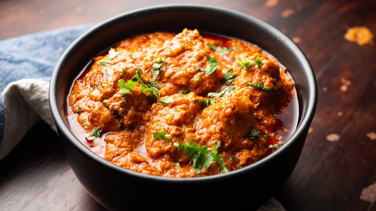 A vibrant bowl of creamy curry topped with fresh cilantro, sitting on a wooden surface, exuding rich flavors and spices.