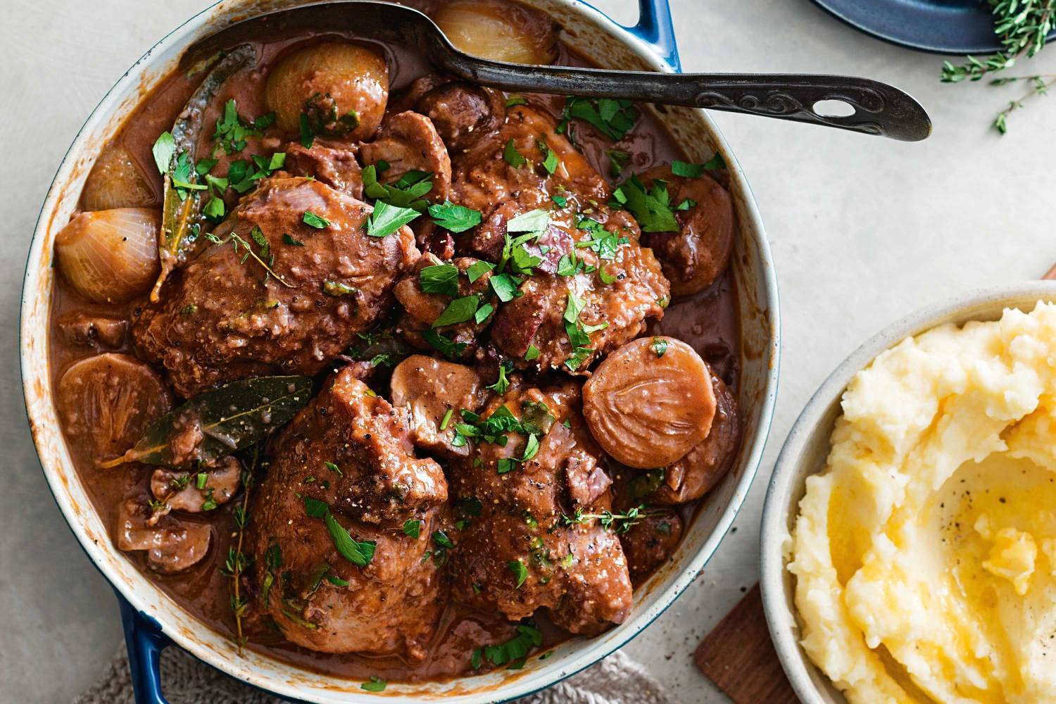 A hearty beef stew with tender meat and onions, garnished with fresh herbs, served alongside creamy mashed potatoes.
