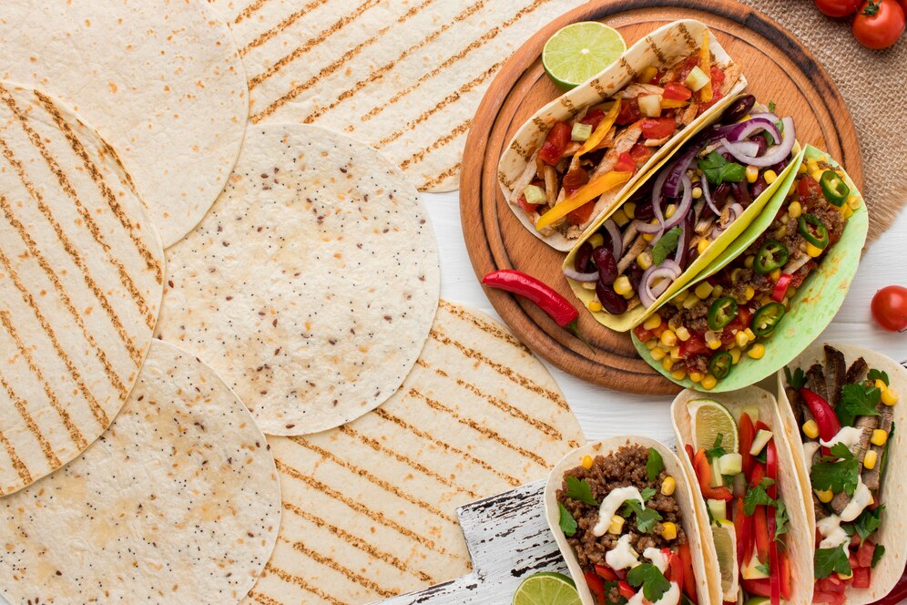 A vibrant array of tacos filled with fresh ingredients, surrounded by grilled tortillas and garnished with lime and chili.