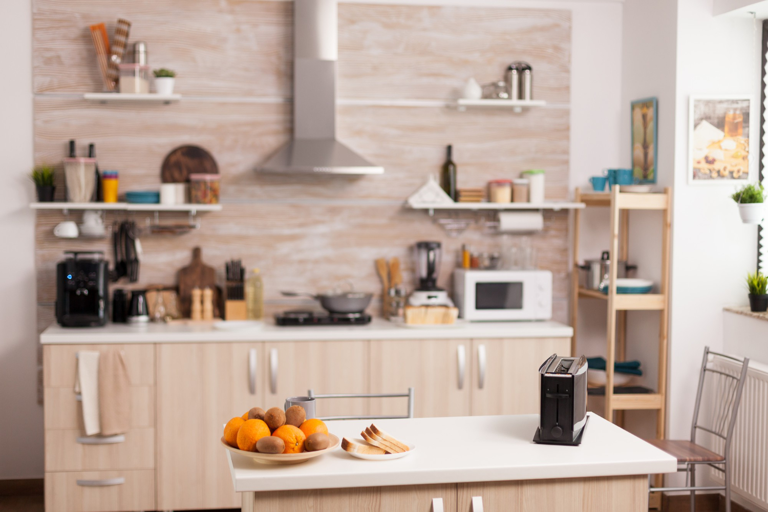 A modern kitchen with light wooden cabinets, a sleek stove, and a countertop featuring a bowl of fruits and a toaster.