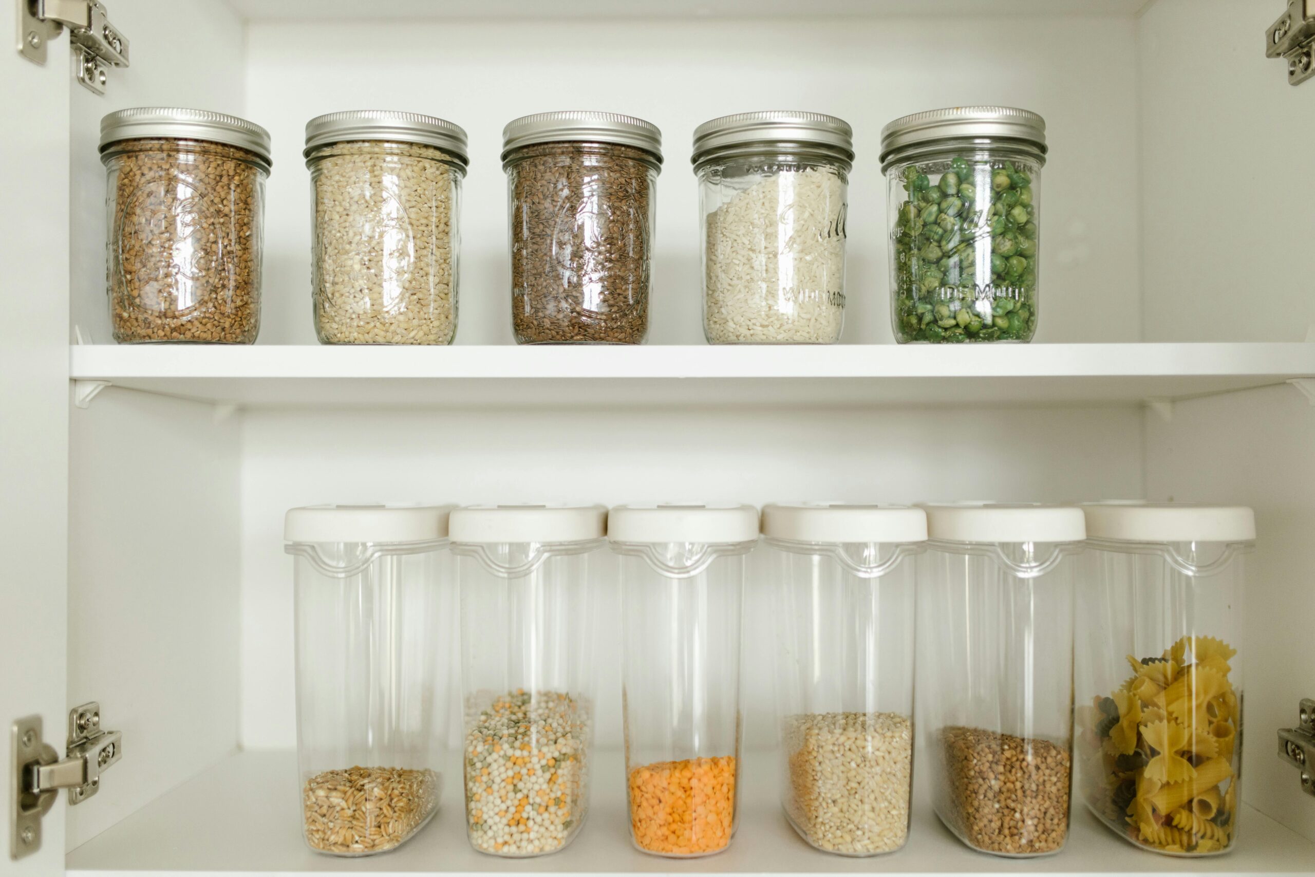 A neatly organized pantry shelf features glass jars of grains and legumes, alongside clear containers filled with various dry goods.