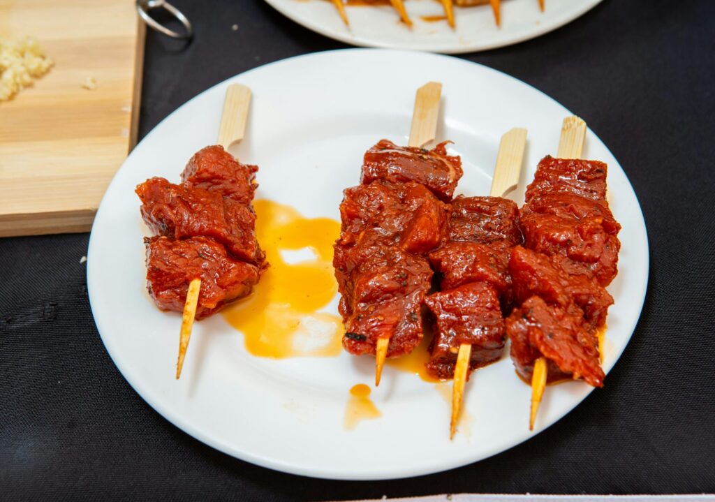 Four skewered pieces of glazed grilled beef on a white plate, with a small pool of sauce underneath.