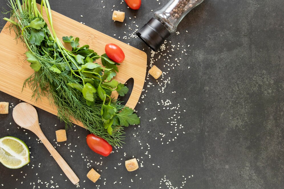 Fresh herbs, cherry tomatoes, and lime on a cutting board, surrounded by spices and seasonings on a dark countertop.
