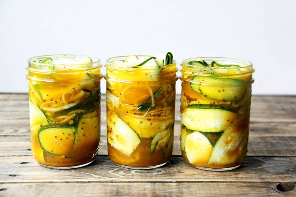 Three jars filled with pickled cucumbers and vibrant yellow brine, arranged on a wooden surface.