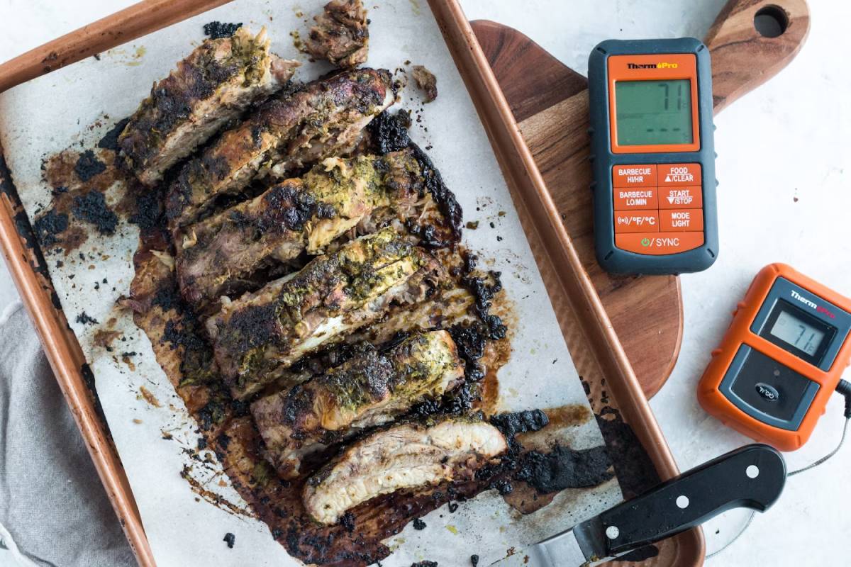 Sliced grilled ribs on a tray with a digital food thermometer and a carving knife.