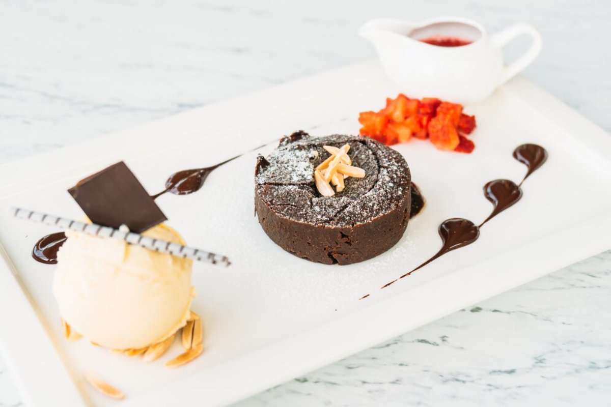 Decadent chocolate lava cake with powdered sugar and almonds, served alongside vanilla ice cream and berry sauce.