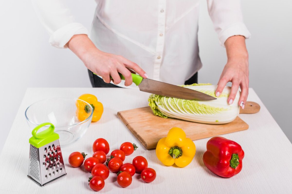Person preparing vegetables, slicing cabbage on a cutting board, surrounded by tomatoes and bell peppers.