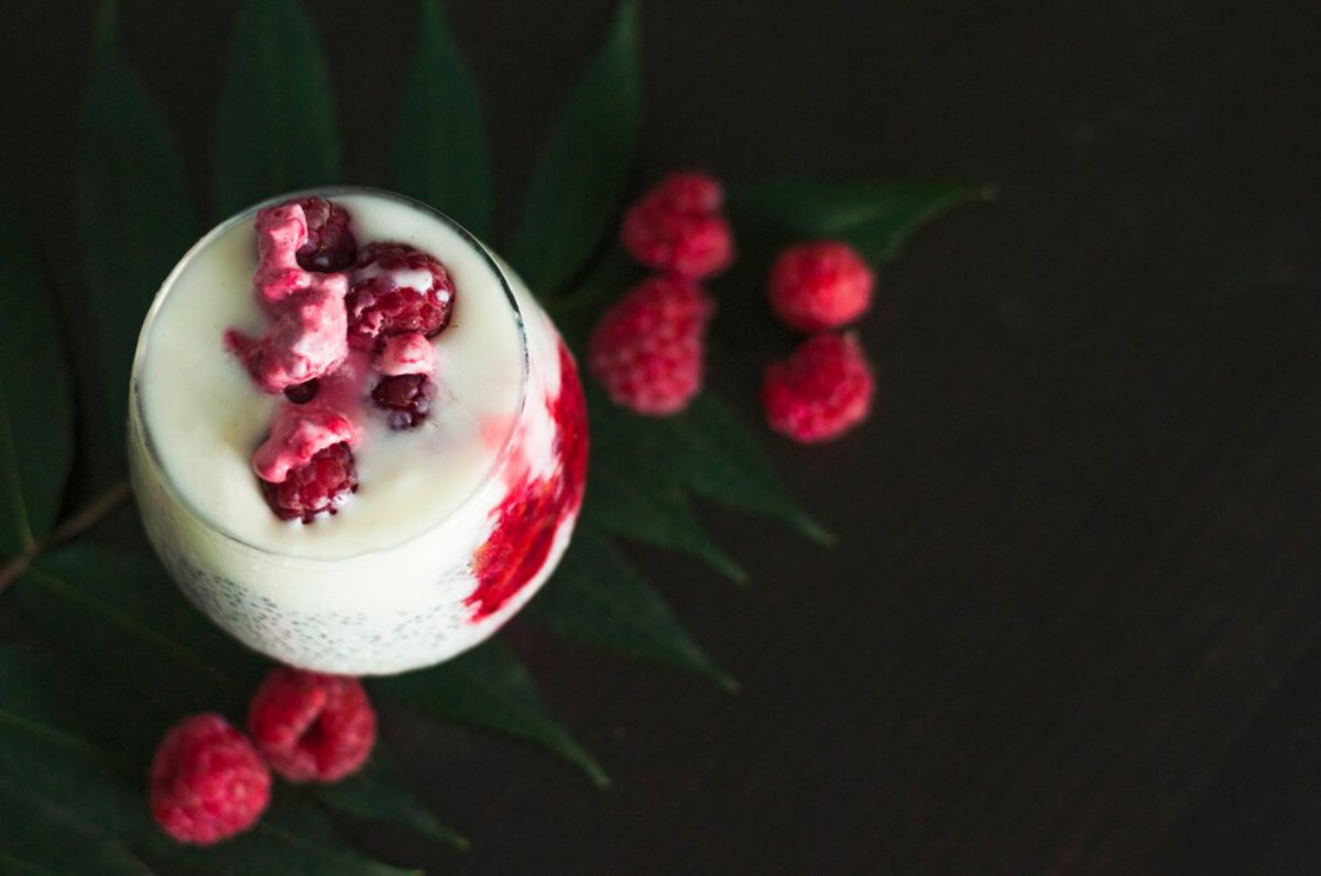 A yogurt parfait with raspberries on a dark background decorated with green leaves.