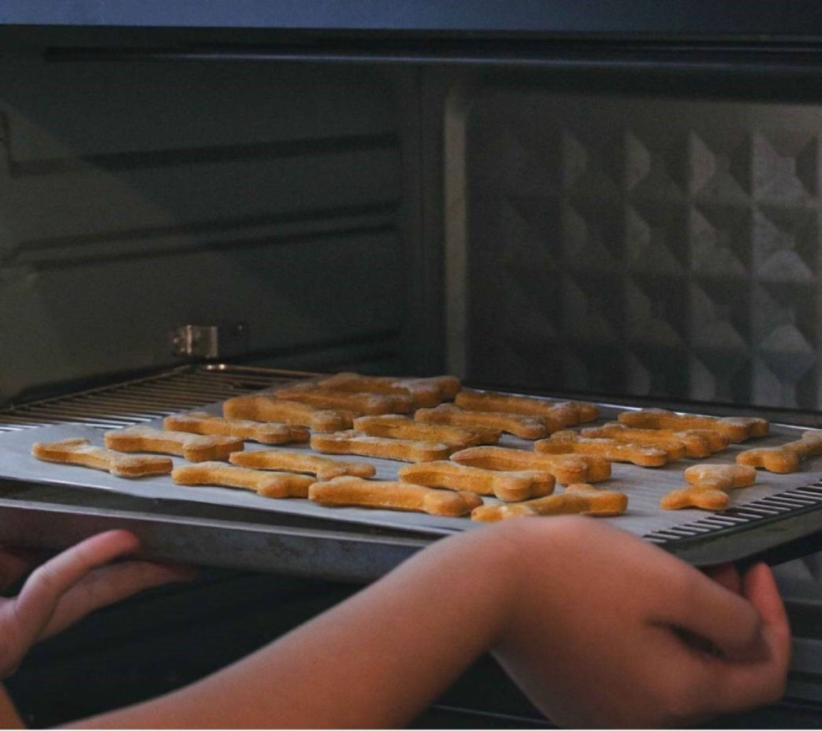 Person placing a tray of shaped chicken nuggets into an oven.