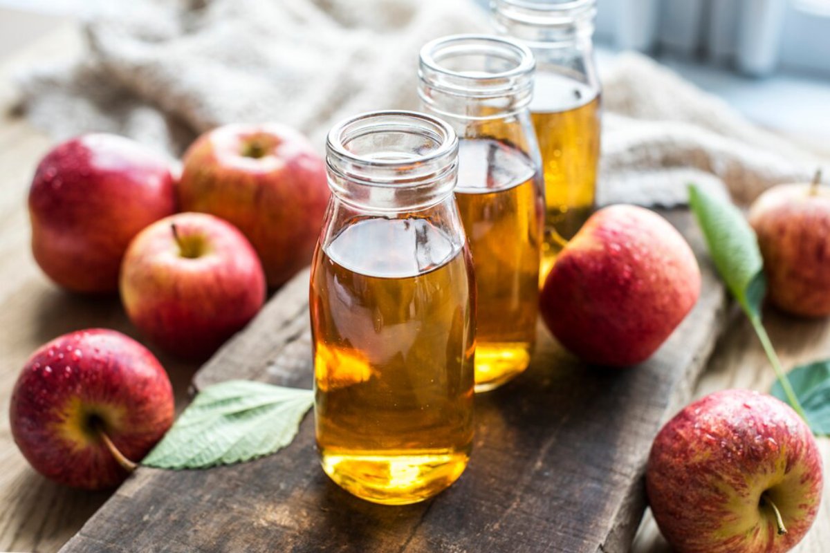 Three glass bottles of apple juice with fresh red apples on a wooden surface.