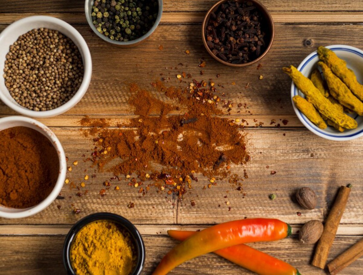 Various spices and vegetables displayed on a wooden table, including turmeric, chili flakes, and carrots.