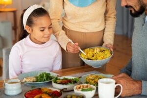 A woman serves a vibrant bowl of rice to a child at the table, surrounded by plates of fresh salads and various colorful dishes.