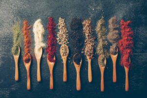 Various colorful spices and herbs arranged in wooden spoons on a dark surface.