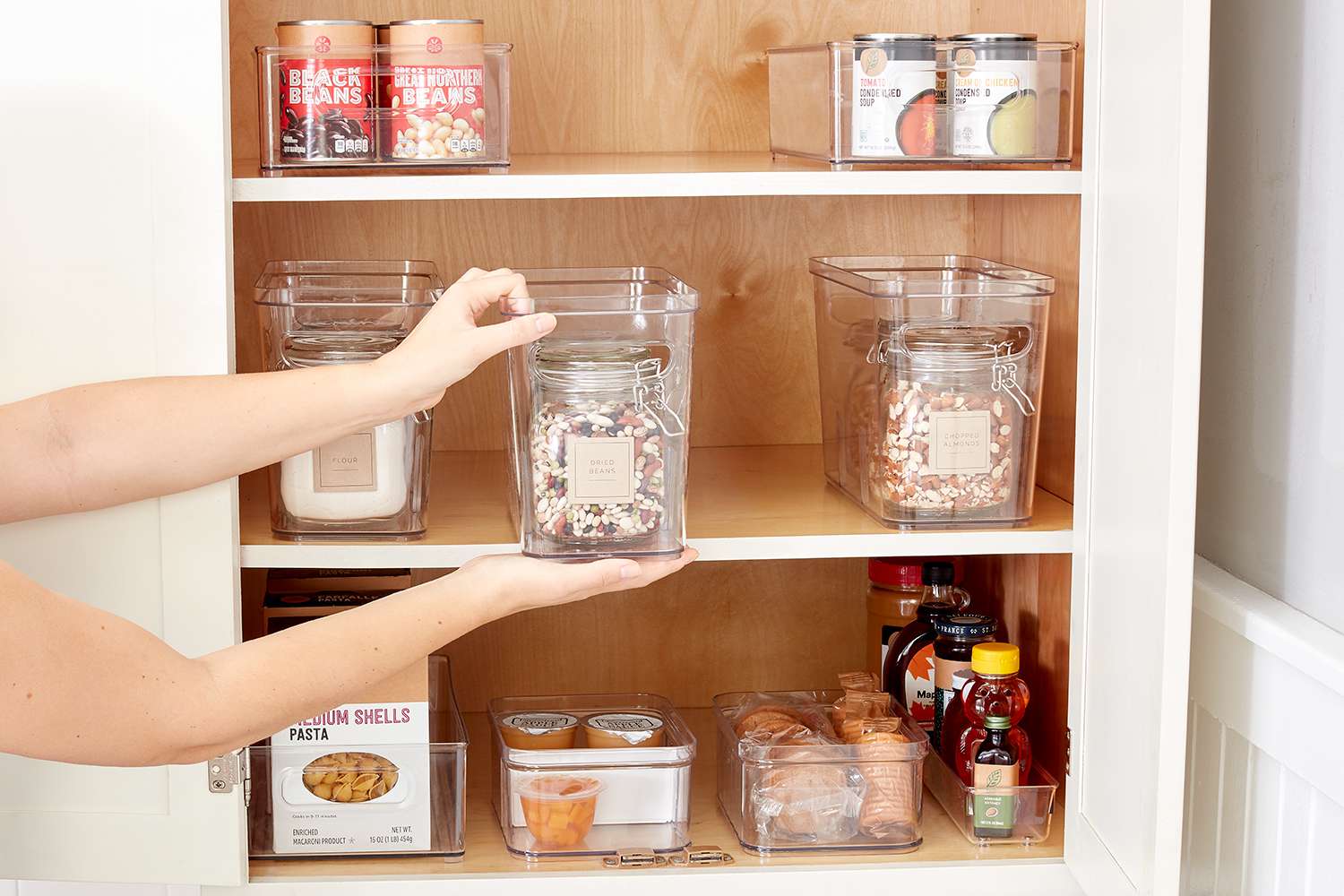 A woman interacts with a cabinet, revealing jars and containers inside, highlighting her effort in organizing kitchen supplies.